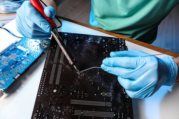 Technician repairing electronic circuit board with soldering iron at table, closeup