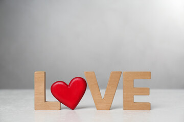 Word Love made of wooden letters and red decorative heart on light table