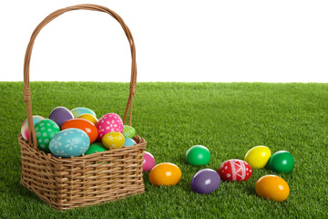 Wicker basket with Easter eggs on green grass against white background. Space for text