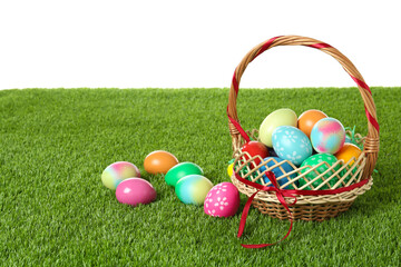 Wicker basket with Easter eggs on green grass against white background. Space for text