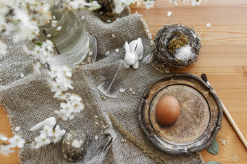 Natural Easter eggs, bunnies, feathers, nest and cherry blooming branch with petals on rustic linen