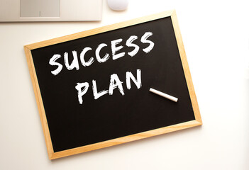 Text SUCCESS PLAN written in chalk on a slate board. Office desk.