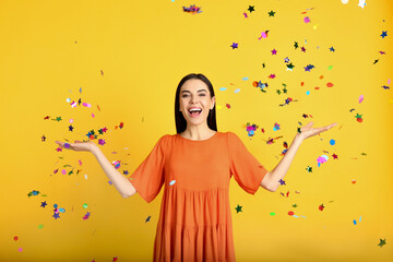 Emotional woman and falling confetti on yellow background