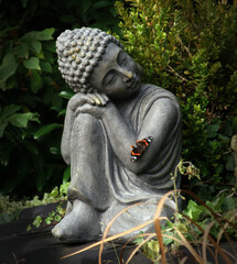 Fototapeta na wymiar Buddha statue in the garden with a butterfly on his arm. This posture represents restfulness and tranquility gained through meditation.