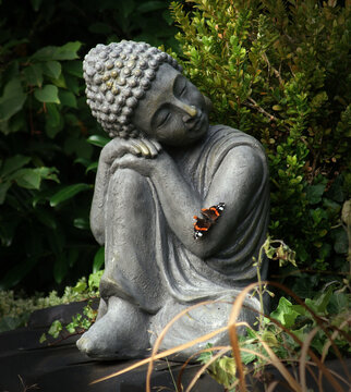 Buddha statue in the garden with a butterfly on his arm. This posture represents restfulness and tranquility gained through meditation.