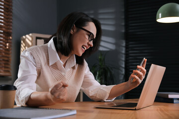 Emotional businesswoman with smartphone near laptop in office. Online hate concept