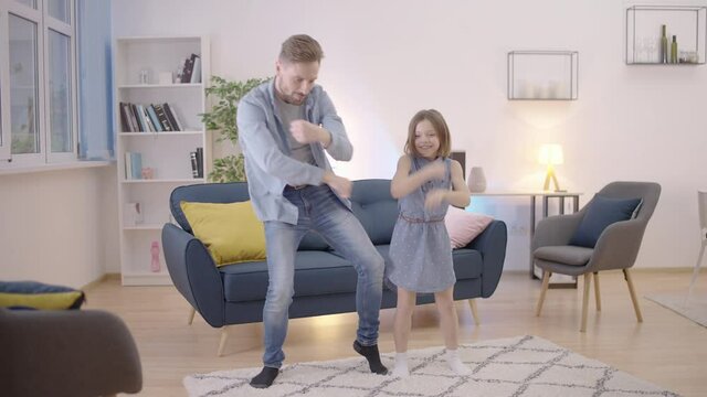 Glad child and dad dancing together at home, enjoying free time together, family