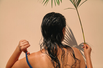 Woman under palm tree takes off her swimsuit. Back view