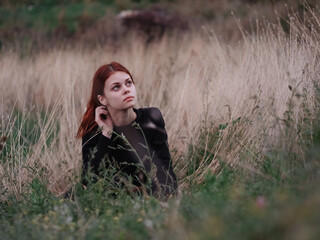 red-haired woman in a black dress lies in a field on dry grass 