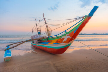 A traditional Sri Lankan fishing catamaran boat during a colourful sunrise or sunset on Weligama, Beach in Sri Lanka. - obrazy, fototapety, plakaty