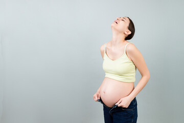 pregnant woman in unzipped jeans showing her naked abdomen at colorful background with copy space