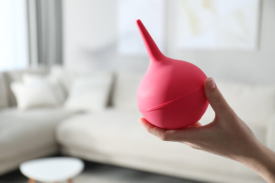 Woman holding pink enema at home, closeup. Space for text