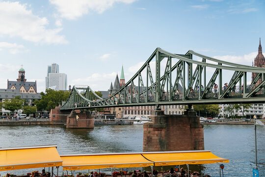 Historical pedestrian Eiserner Steg, Iron footbridge over the Main river, consists of riveted steel trusses, two bridge piers, love locks, sunny summer day, Frankfurt am Main, Germany