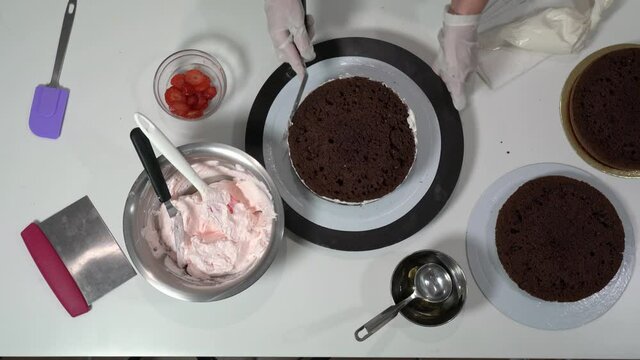 Front shot of a baker using an icing spatula to carefully touch up sides of cream covered cake.