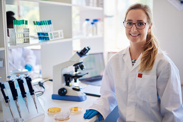 Smiling female lab technician working with samples and a microscope