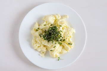 Scrambled eggs with microgreens on a white plate. Close up.
