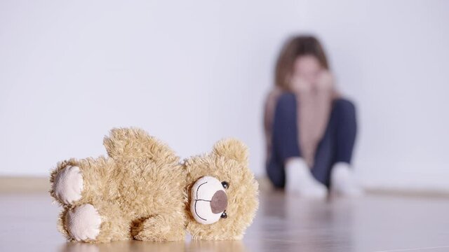 Teddy bear toy on the floor, crying little girl on background, childhood trauma