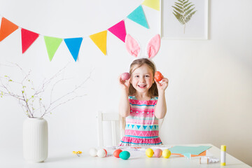 happy girl with bunny ears and easter eggs in her hands. materials for art craft creativity on table. home decor