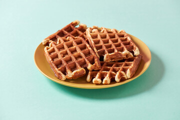 Homemade waffles. Freshly baked Belgian waffles with sugar on yellow plate isolated over blue background, traditional Belgian dessert