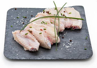 Raw chicken wings marinated with salt, pepper and chives on slate board isolated on white background. © PhotoStk
