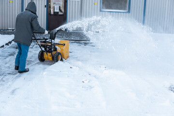 Man cleaning driveway with snow machines after a snow storm. Snow removal equipment working on the street. Cleaning of streets from snow. It's snowing.