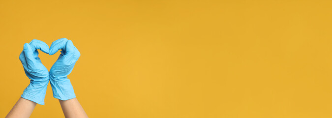 Doctor in medical gloves showing heart with hands on yellow background, closeup. Banner design with space for text