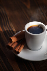 A cup of aromatic black coffee. Morning espresso or Americano coffee for breakfast in a beautiful cup. Cinnamon sticks. Wooden background. 