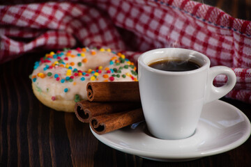A cup of aromatic black coffee with a donut in the background. Morning espresso or Americano coffee for breakfast in a beautiful cup. Wooden background. Couple with coffee. 