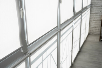 White fabric roller blinds on the plastic window on a balcony in the living room.