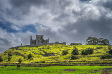 Beautiful Rock of Cashel castle with cattle grazing on field and dramatic dark storm clouds in...