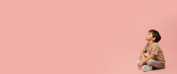 Dreaming, flyer. Happy, smiley little caucasian boy isolated on pink studio background with copyspace for ad. Looks happy, cheerful. Childhood, education, human emotions, facial expression concept.