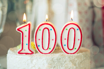 Birthday candle as number one hundred on top of sweet cake on the table, 100th birthday - 419623715