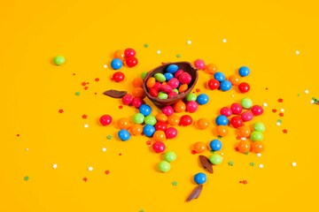 Chocolate Easter eggs with colored candies on a yellow background.