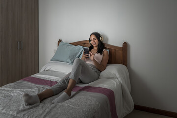 Naklejka premium Content woman listening to music and browsing smartphone on bed