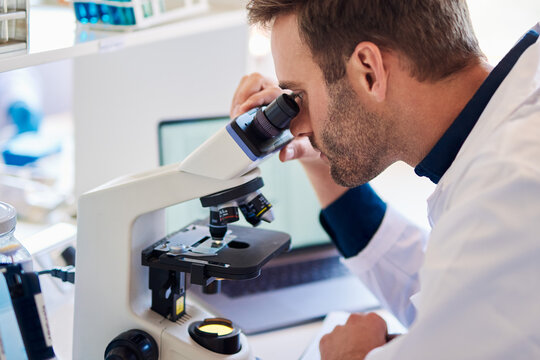 Male lab technician analyzing samples under a microscope