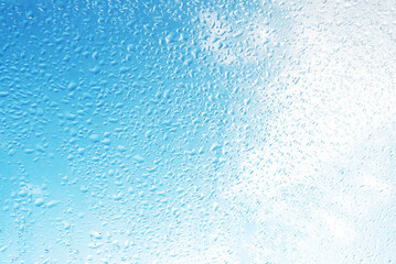 Rain drops on surface of the window glass with sky cloud background. Natural pattern of water drops on glass