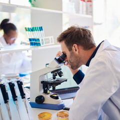 Male lab technician analyzing samples under a microscope