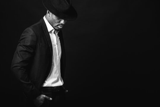 Portrait of attractive, cute, stylish professional African American businessman in stylish suit, white shirt and black hat, isolated on dark background. Low key. Selective focus