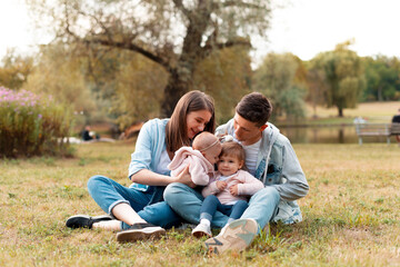 Naklejka na ściany i meble Wonderful young family is sitting on grass spending time together smiling.