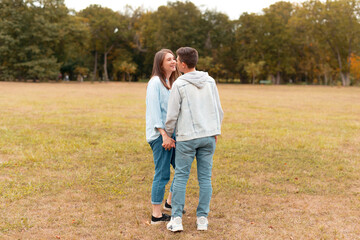 Fototapeta premium Young cute couple is holding hands and looking at each other outdoors in a park