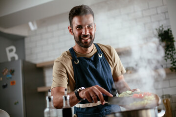 Happy smiling man preparing tasty meal. Young man cooking in the kitchen.