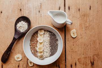 Frühstücktisch mit Müslischale und gesunden Zutaten wie Haferflocken, Leinsamen, Chiasamen, Bananen und Pflanzenmilch