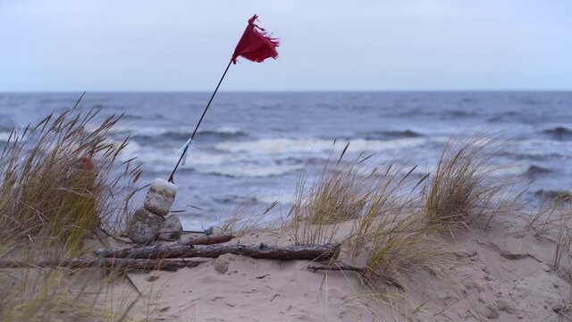 Red flag in the sand dunes of the Baltic. People walk along the coast of the Gulf of Riga in a strong storm at sea. Latvia