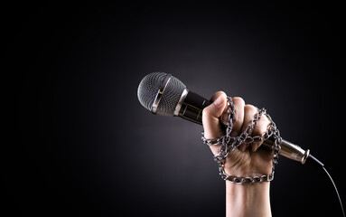 World press freedom day concept. Hand holding a microphone with chain on dark background, symbol of press freedom of speech freedom.