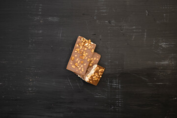 a lot of different types of chocolate and various ingredients such as nuts and cocoa powder lie on a black wooden plate photo taken from above