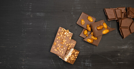 a lot of different types of chocolate and various ingredients such as nuts and cocoa powder lie on a black wooden plate photo taken from above
