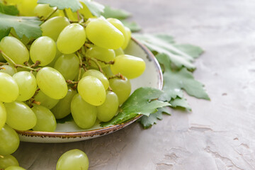Plate with ripe green grapes on grunge background, closeup