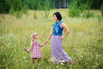 Naklejka premium Smiling mother and daughter in the meadow enjoy a beautiful summer day