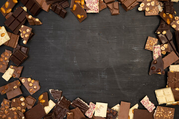 a lot of different types of chocolate and various ingredients such as nuts and cocoa powder lie on a black wooden plate photo taken from above