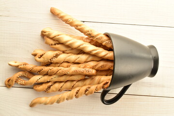 Grissini bread sticks with sesame seeds with a ceramic cup, close-up, on a wooden table.